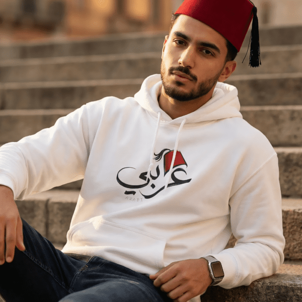 Arabic man wearing white color of Arabi hoodie for men with the Arabic word "عربي" in modern Arabic calligraphy design, and a classic red Tarboosh on his head