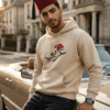 Arabic man wearing sand color of Arabi hoodie for men with the Arabic word "عربي" in modern Arabic calligraphy design, and a classic red Tarboosh on his head