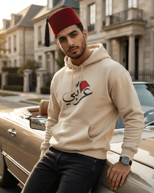 Arabic man wearing sand color of Arabi hoodie for men with the Arabic word "عربي" in modern Arabic calligraphy design, and a classic red Tarboosh on his head