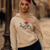 Arabic woman wearing beige hijab and sand color of Arabiya hoodie for women with the Arabic word "عربية" in modern Arabic calligraphy design