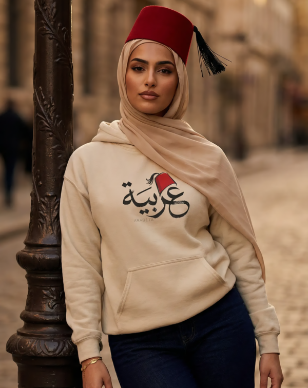 Arabic woman wearing beige hijab and sand color of Arabiya hoodie for women with the Arabic word "عربية" in modern Arabic calligraphy design