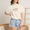 Woman wearing a cute Arabic travel t-shirt with the phrase "يلا نضيّع شوي" on Comfort Colors 1717 Ivory.