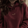 Woman wearing oversized maroon Arabic hoodie with gold embroidery
