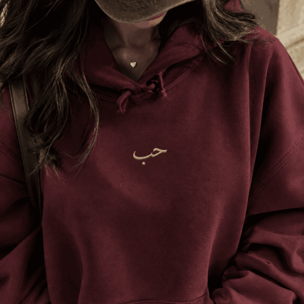 Woman wearing oversized maroon Arabic hoodie with gold embroidery