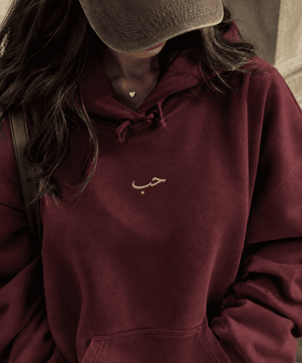 Woman wearing oversized maroon Arabic hoodie with gold embroidery